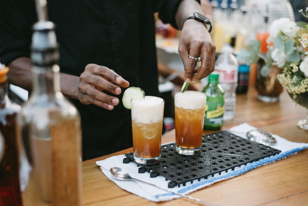 Bartender puts a cucumber slice on the side of a drink at a wedding