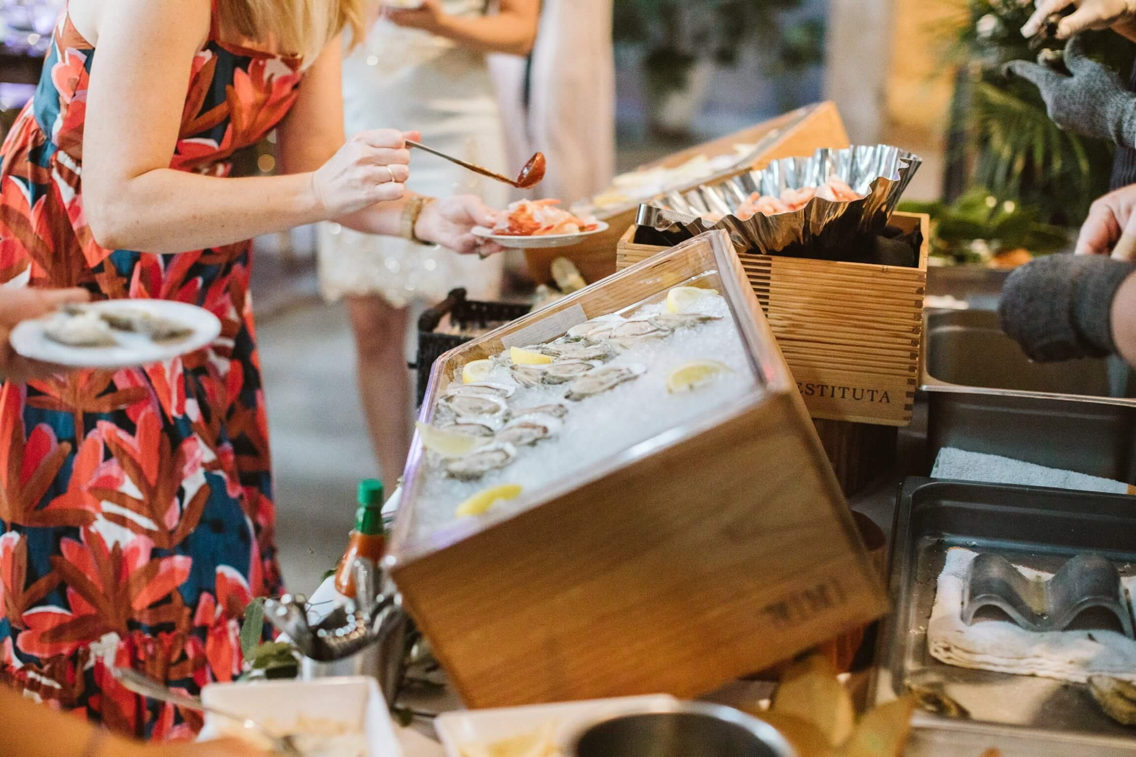 Wedding guest serves herself cocktail sauce over shrimp next to oysters on ice