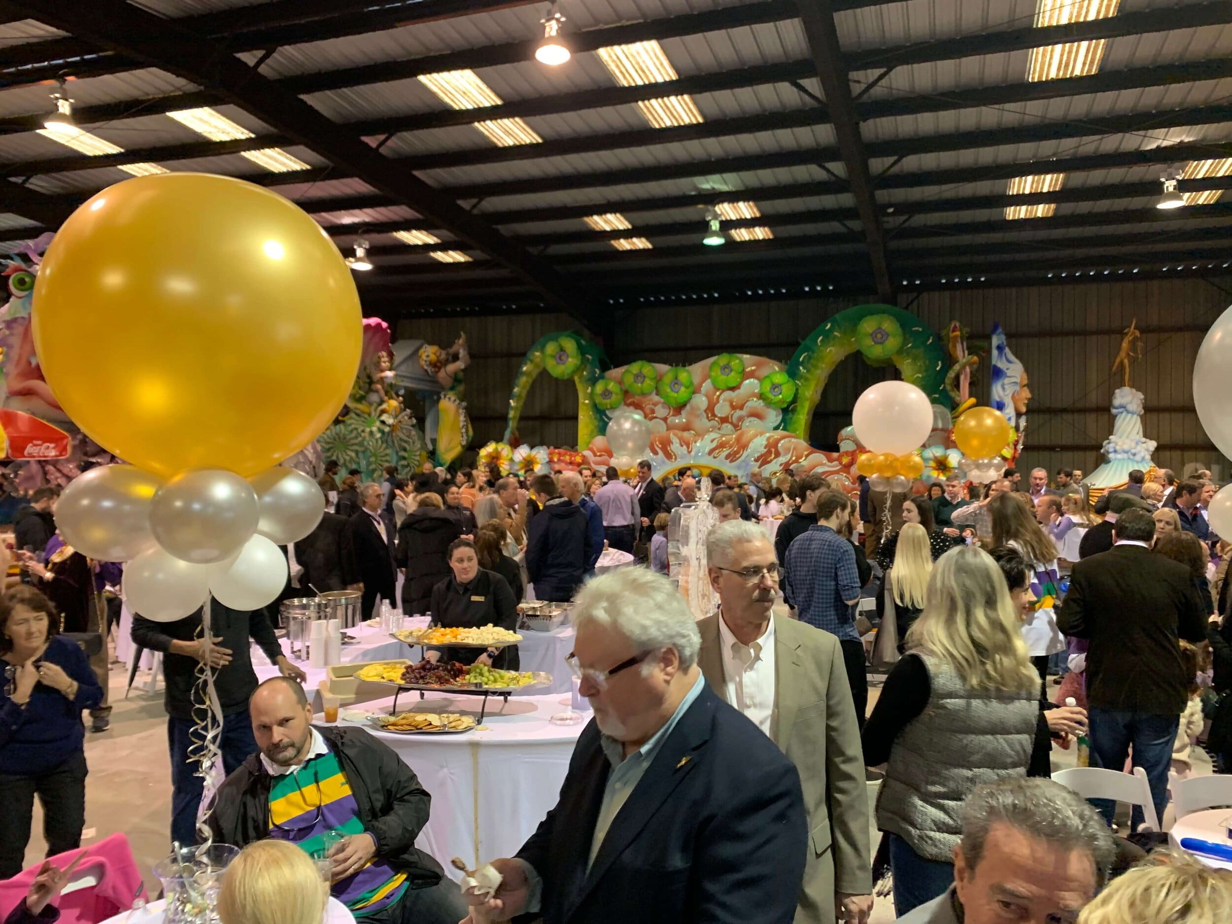 Guests at New Orleans Hermes Party event, with Mardi Gras floats and balloons