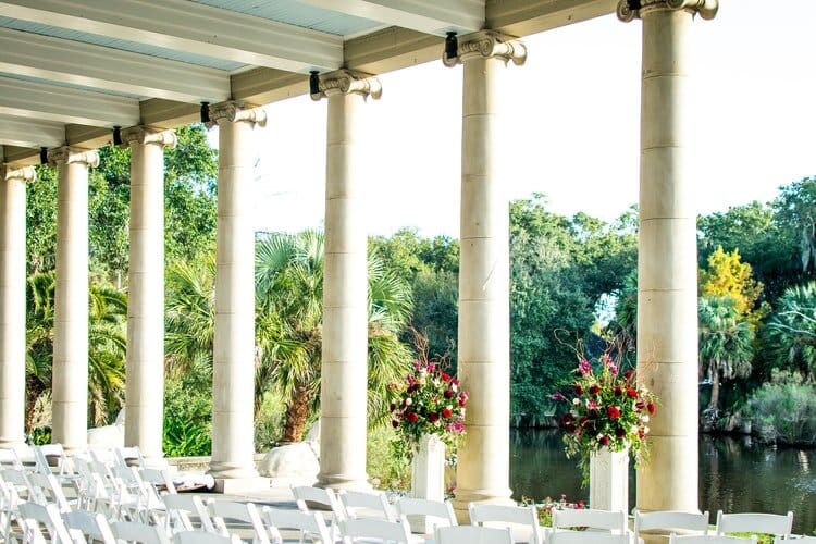 Wedding venue with white chairs under a columned roof facing the water