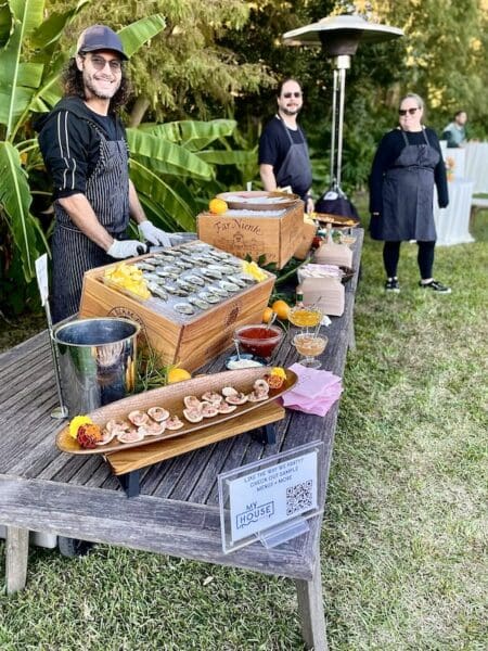 Questions to ask catering services represented by Elysian Events Catering co-founders standing by an oyster bar at an event.