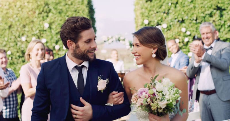 Cropped shot of an affectionate young newlywed couple leaving their wedding venue with their guests clapping in the background