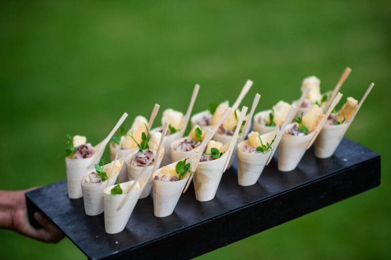 Fried Calamari Scampi Appetisers canapes being presented in bamboo cones and served at a party with selective focus. It is being served at a wedding party. A waiter is holding the tray with canapes.