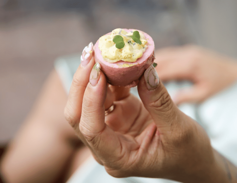 Hand holding a deviled egg shows a great pink baby shower catering idea