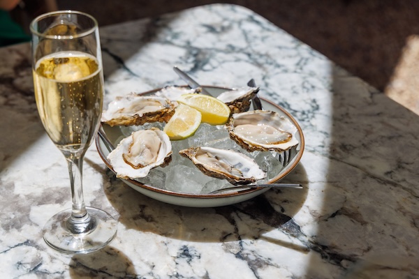 Fresh oysters on ice with champagne on a sunlit table, showcasing what goes good with oysters